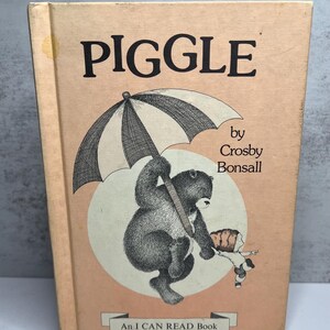 May include: A vintage children's book titled "Piggle" with a light peach cover. The cover features a black and white illustration of a bear holding an umbrella with a child. The text "Piggle" is in large, bold letters.