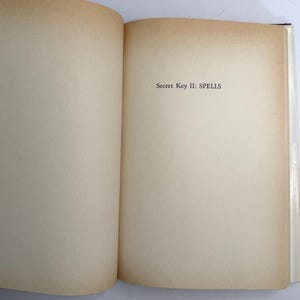 May include: Open book with aged, off-white pages. The text "Secret Key II: SPELLS" is printed in black near the top of the right-hand page. The edges of the pages have a warm, brown tone.