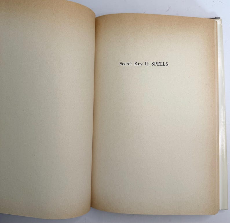May include: Open book with aged, off-white pages. The text "Secret Key II: SPELLS" is printed in black near the top of the right-hand page. The edges of the pages have a warm, brown tone.