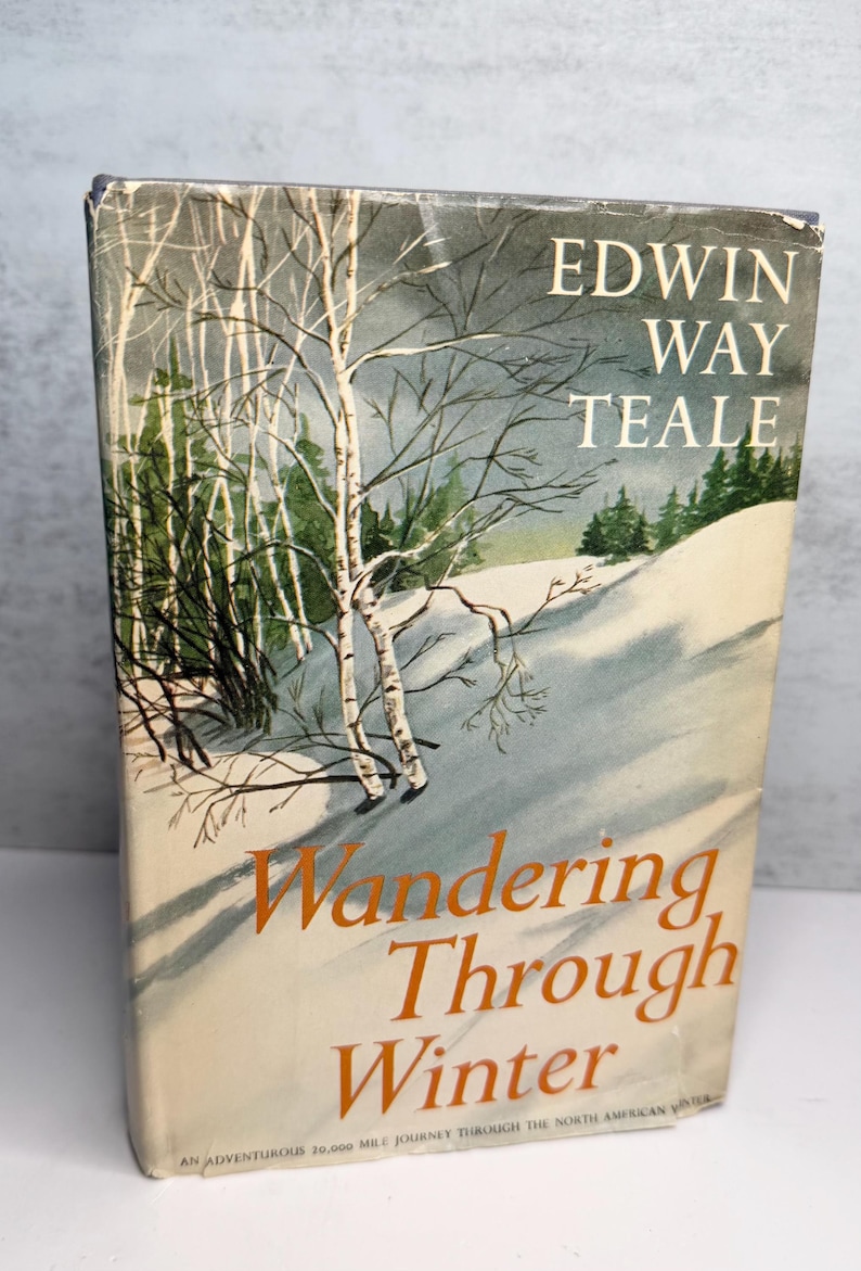 May include: A vintage book cover with a winter landscape illustration. The title "Wandering Through Winter" is in orange, with the author's name, Edwin Way Teale, above. The cover depicts a snowy scene with trees.