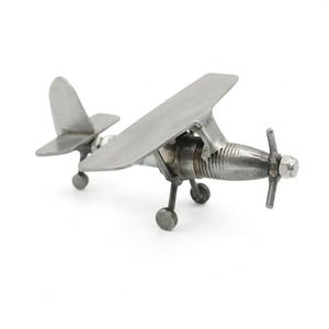 Op de afbeelding: Een klein, zilverkleurig vliegtuigmodel met een propeller en twee vleugels. Het miniatuurvliegtuig heeft een gedetailleerd ontwerp, inclusief wielen en een staartvin. Het model is gemaakt van metaal en staat op een witte achtergrond.