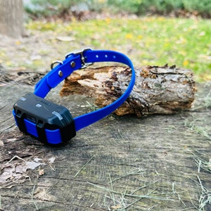 May include: A blue dog training collar with a black Garmin device attached. The collar is lying on a wooden surface.