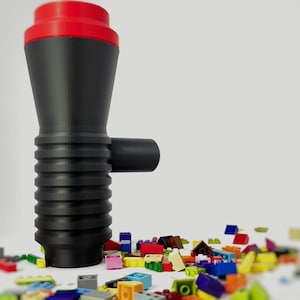 May include: A black and red plastic toy with a ribbed texture and a small side pipe. The toy is surrounded by a pile of colorful plastic building blocks.