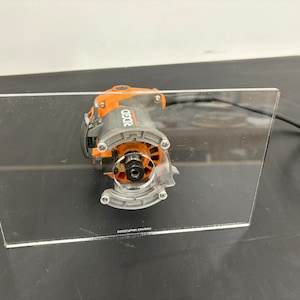 Peut inclure: Une d&eacute;fonceuse noire et orange avec une base en plastique transparente. La d&eacute;fonceuse est pos&eacute;e sur une base en acrylique transparente. La base porte l'inscription "RIDGID".