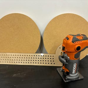K&ouml;nnte beinhalten: Nahaufnahme eines Fr&auml;sers mit schwarzem und orangefarbenem Geh&auml;use, einer transparenten Basis und dem Schriftzug "RIDGID" auf der Seite. Der Fr&auml;ser steht auf einer schwarzen Oberfl&auml;che vor zwei runden Holzst&uuml;cken.