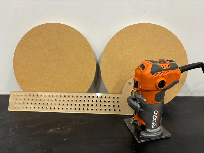 K&ouml;nnte beinhalten: Nahaufnahme eines Fr&auml;sers mit schwarzem und orangefarbenem Geh&auml;use, einer transparenten Basis und dem Schriftzug "RIDGID" auf der Seite. Der Fr&auml;ser steht auf einer schwarzen Oberfl&auml;che vor zwei runden Holzst&uuml;cken.