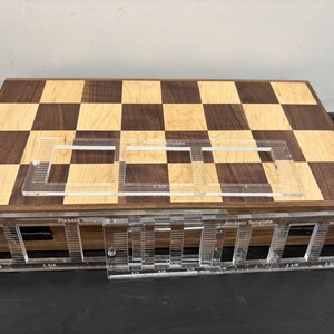 May include: A wooden chessboard with a checkerboard pattern of light and dark wood. A clear plastic template with the text "Pocket Template" is placed on top of the chessboard. The template has markings for pocket placement.