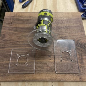 Könnte beinhalten: Eine lindgrüne und dunkelgraue Ryobi Kantenfräse mit montierter runder Grundplatte aus klarem Acryl, begleitet von zwei weiteren Grundplatten aus klarem Acryl, einer quadratischen und einer rechteckigen, jeweils mit vier vorgebohrten Löchern.