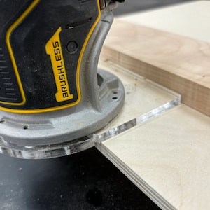 May include: A close-up of a yellow and black electric router with the word "BRUSHLESS" printed on the side. The router is being used to cut a piece of wood with a clear acrylic guide.