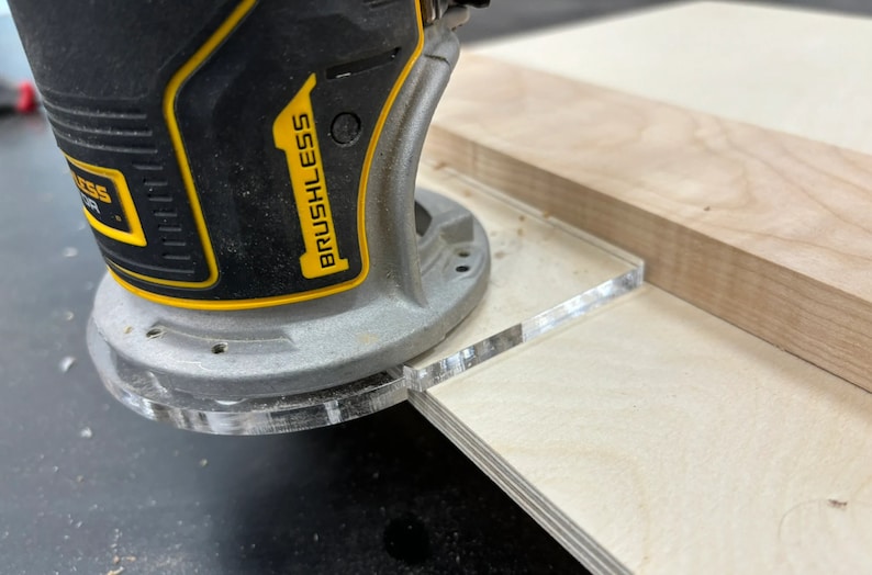 May include: A close-up of a yellow and black electric router with the word "BRUSHLESS" printed on the side. The router is being used to cut a piece of wood with a clear acrylic guide.