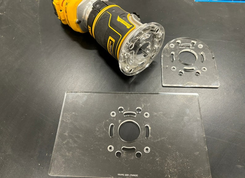 May include: A clear plastic router template with a circular cutout and multiple smaller holes. The template is designed to be used with a router to create precise cuts in wood or other materials.