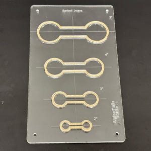 K&ouml;nnte beinhalten: Eine transparente Kunststoffschablone mit vier verschiedenen Gr&ouml;&szlig;en von Barbell-Einlegemustern. Die Schablone ist mit "Barbell Inlays" beschriftet und enth&auml;lt Ma&szlig;e in Zoll: 5", 4", 3" und 2". Die Schablone ist auch mit "Alpine Trails Studio 52" beschriftet.
