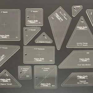 Peut inclure: Ensemble de gabarits de quilting en acrylique transparent de différentes formes, dont des carrés, des triangles et des rectangles. Chaque gabarit est étiqueté avec ses dimensions en cm et le logo "Alpine Trails Studio".