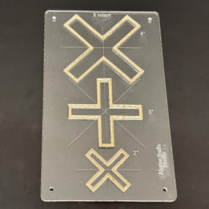 K&ouml;nnte beinhalten: Eine transparente Acryl-Schablone mit drei goldfarbenen X-Formen. Die Schablone ist mit "X Inlays" beschriftet und hat Ma&szlig;e in Zoll. Das gr&ouml;&szlig;te X ist 4 Zoll breit, das mittlere X ist 3 Zoll breit und das kleinste X ist 2 Zoll breit. Die Schablone wird von Alpine Trails Studio hergestellt.