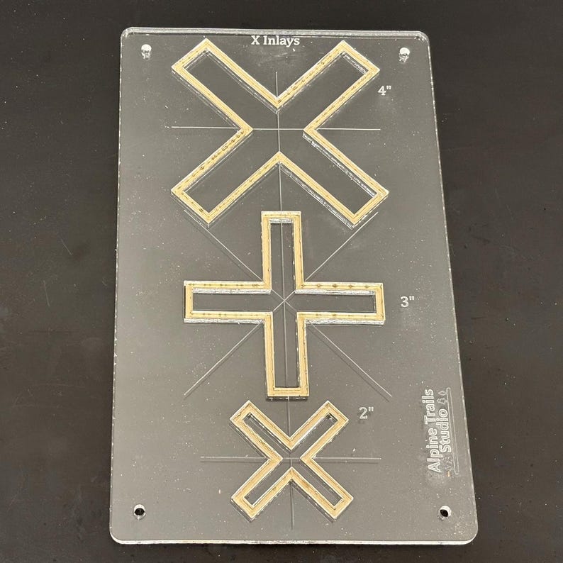 K&ouml;nnte beinhalten: Eine transparente Acryl-Schablone mit drei goldfarbenen X-Formen. Die Schablone ist mit "X Inlays" beschriftet und hat Ma&szlig;e in Zoll. Das gr&ouml;&szlig;te X ist 4 Zoll breit, das mittlere X ist 3 Zoll breit und das kleinste X ist 2 Zoll breit. Die Schablone wird von Alpine Trails Studio hergestellt.