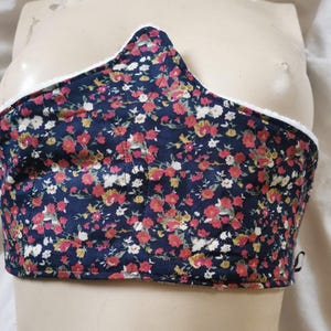 May include: A dark blue fabric corset with a white trim and a floral print. The corset is made of a soft, comfortable material and has a unique design.