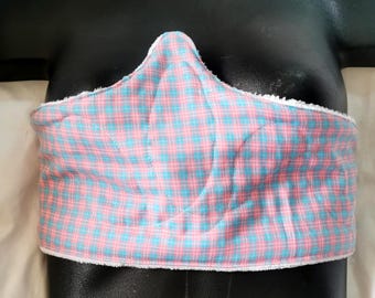 Może przedstawiać: Wyściełany bandaż na klatkę piersiową z różowo-niebieskim wzorem w kratę. Opatrunek ma białe, puszyste wykończenie wzdłuż krawędzi. Artykuł jest przeznaczony do dopasowania wokół klatki piersiowej.