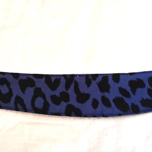 Peut inclure: Un bandeau imprimé léopard bleu et noir. Le bandeau est incurvé et possède un dessous blanc. Une petite étiquette rose avec du texte est cousue à l'extrémité du bandeau.