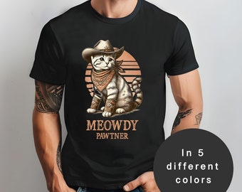 Peut inclure: Un t-shirt noir avec une illustration de dessin animé d'un chat portant un chapeau de cowboy et un bandana. Le texte "MEOWDY PAWTNER" est imprimé sous le chat.