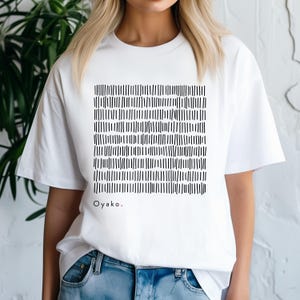 May include: White t-shirt featuring a black and white abstract design of vertical lines. The design is a square pattern. The word "Oyako." is printed in black with a red period at the end.