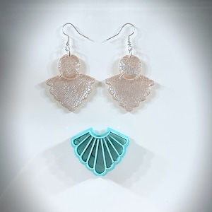 May include: A pair of gold-toned earrings with a fan-shaped design. The earrings are made of two layers of metal, with the top layer being a circle and the bottom layer being a fan. The earrings are hanging from silver hooks. A turquoise plastic fan-shaped mold is also shown in the image.