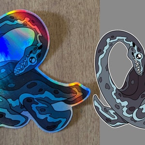 Pu&ograve; includere: Un adesivo olografico di un serpente marino blu e verde con contorno nero. Il serpente &egrave; arrotolato in un cerchio con la testa rivolta verso lo spettatore. L'adesivo &egrave; su una superficie di legno.