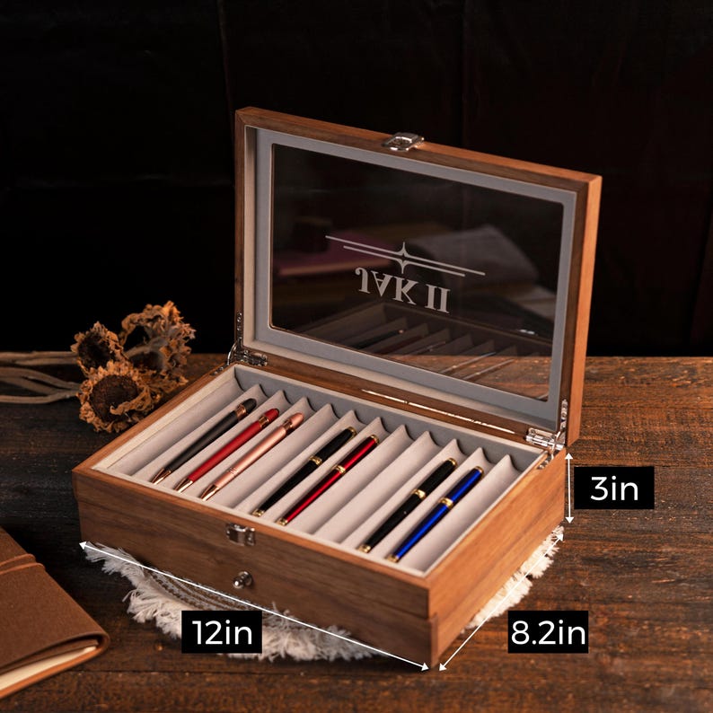 Może przedstawiać: Drewniane etui na długopisy ze szklaną pokrywą, mieszczące kilka długopis&oacute;w w r&oacute;żnych kolorach. Etui ma 30.5 cm długości, 20.8 cm szerokości i 7.6 cm wysokości. Tekst "IVK II" jest widoczny.
