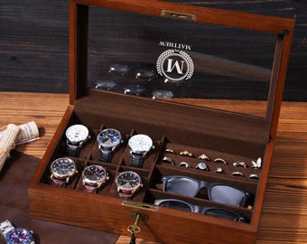 May include: A wooden watch and jewelry box with a glass top, displaying several watches, rings, and sunglasses. The box is brown with a dark interior and a lock. The glass top has the name "MATTHEW" and the letter "M" printed on it.