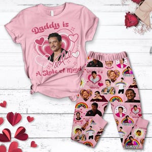 Peut inclure: Ensemble pyjama rose composé d'un t-shirt à manches courtes et d'un pantalon long. Le t-shirt présente un motif graphique d'un homme avec le texte "Daddy is a State of Mind". Le pantalon a un motif répété du même homme et du texte "Daddy's Little Girl".