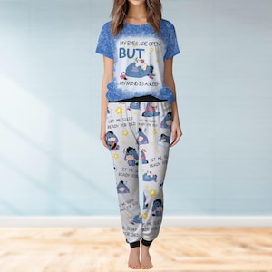 May include: A two-piece pyjama set with a blue and white top and grey trousers. The top features the text "MY EYES ARE OPEN BUT MY MIND IS ASLEEP" with a cartoon character. The trousers have a repeating pattern of the same character and text "LET ME SLEEP READY FOR BED".