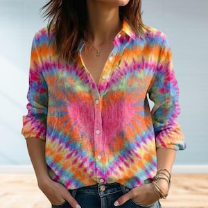 Może przedstawiać: Zapinana na guziki koszula z żywym wzorem tie-dye w odcieniach różu, pomarańczy, żółci i niebieskiego. Koszula z długim rękawem ma klasyczny kołnierzyk i jest wykonana z lekkiego materiału. Koszula jest rozpięta przy dekolcie.
