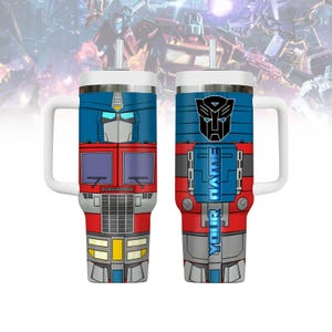 May include: A stainless steel travel mug with a blue, red, and gray design featuring the Transformers character Optimus Prime. The mug has a handle and a straw lid. The text "YOUR NAME" is printed on the side of the mug.