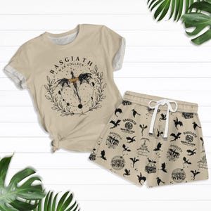 Peut inclure: Un t-shirt beige avec un motif de dragon noir et le texte "Basgiath War College". Un short beige avec un motif de dragon noir et le texte "Basgiath War College" et "Fourth Wing".