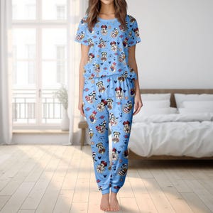 May include: Light blue pyjama set with a repeating pattern of cartoon characters. The short-sleeved top and matching trousers display Mickey Mouse, Minnie Mouse, Donald Duck, and other characters. The pyjamas are made of a soft, comfortable material.