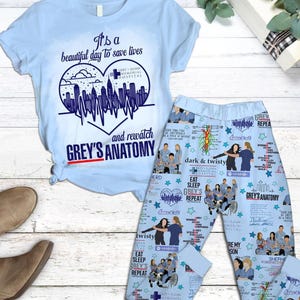 Può includere: Set pigiama Grey's Anatomy azzurro. La maglietta a maniche corte presenta un design a forma di cuore con uno skyline e la scritta "It's a beautiful day to save lives". I pantaloni del pigiama hanno un motivo ripetuto di personaggi e frasi.