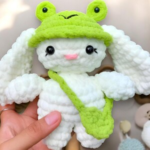 May include: White crocheted bunny with long ears wearing a green crocheted frog hat and a green crocheted bag.