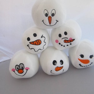 May include: Six white plush snowman ornaments with different facial expressions. Each snowman has black eyes, a black mouth, and an orange carrot nose. Some snowmen have pink cheeks.