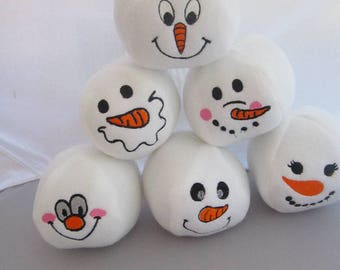 May include: Six white plush snowman ornaments with different facial expressions. Each snowman has black eyes, a black mouth, and an orange carrot nose. Some snowmen have pink cheeks.