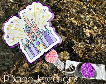 May include: A purple glitter castle-shaped badge holder with a pink glitter bead and a purple glitter charm. The castle is outlined in purple and has a white background with gold glitter fireworks.