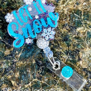 May include: A blue and white glitter "Let it Snow" badge holder with a snowflake design. The badge holder has a clear plastic clip and a blue glitter charm.