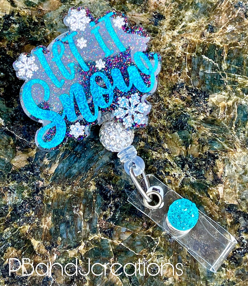 May include: A blue and white glitter "Let it Snow" badge holder with a snowflake design. The badge holder has a clear plastic clip and a blue glitter charm.