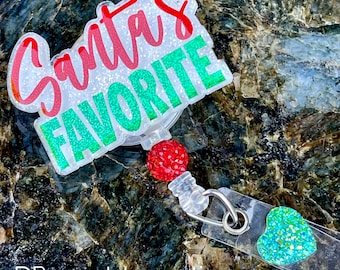 May include: A clear plastic badge holder with a sparkly green and red "Santa's Favorite" design. The holder has a retractable cord with a sparkly red bead and a sparkly green heart charm.