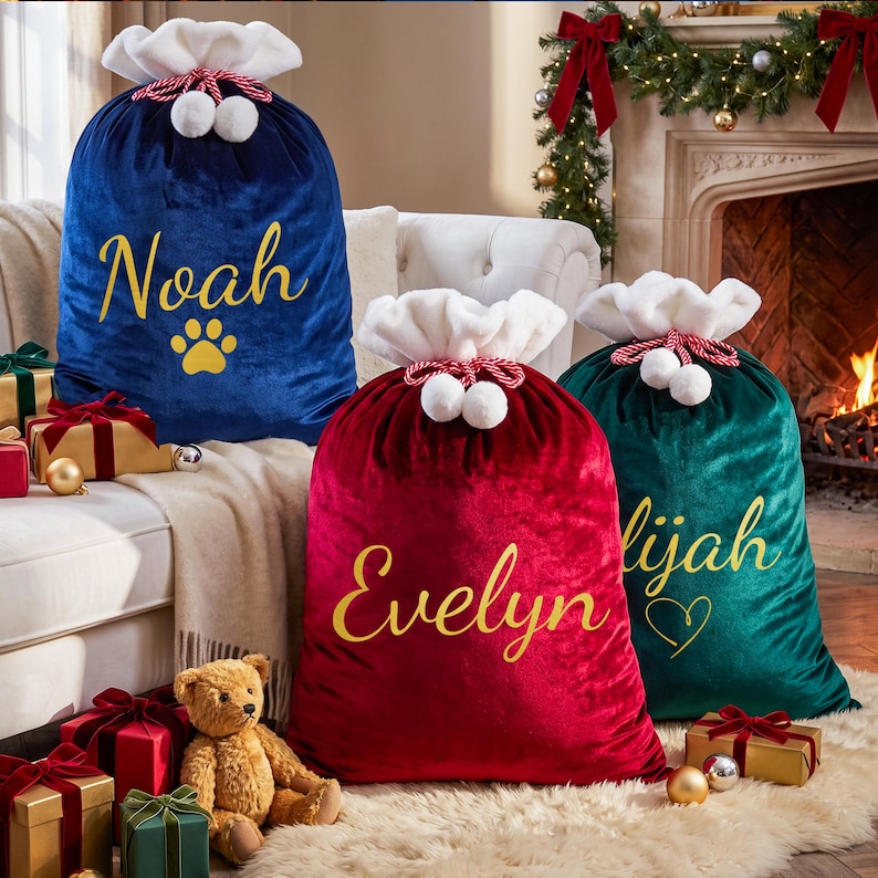 May include: Three large velvet Christmas gift sacks in blue, red, and green. Each sack features a white plush top, a red and white twisted drawstring with pom-poms, and gold script lettering reading Noah, Evelyn, and Elijah with icons.