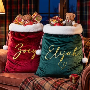 May include: Two large velvet Christmas gift sacks, one deep red with the name Zoey and one dark green with the name Elijah and a heart, both featuring white faux fur trim, red and white twisted rope drawstrings, and plush teddy bears on top.