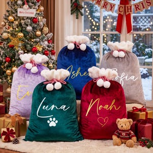 May include: Five velvet Christmas gift sacks in purple, dark blue, gray, dark green, and red. Each sack features a white plush drawstring top with pom-poms and personalized names in script font: Eva, Asher, Sofia, Luna, and Noah.