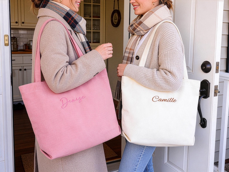 May include: Two tote bags, one pink and one off-white, are held by two people. The pink bag has the name "Denize" embroidered on it, while the off-white bag has "Camille". Both bags have long handles.