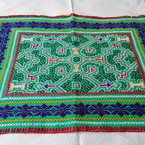 May include: A green, blue, yellow, and red embroidered fabric with a geometric pattern. The fabric has a border with a floral design.