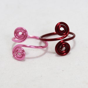 May include: Two wire rings with a spiral design. One ring is pink and the other is red.