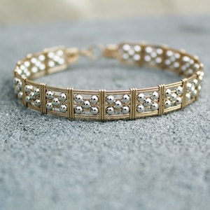 May include: A gold and silver bracelet with a geometric design. The bracelet is made of wire and beads.