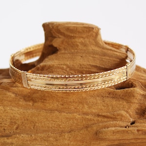 May include: A gold bangle bracelet with multiple strands of wire woven together. The bracelet has a simple, elegant design.